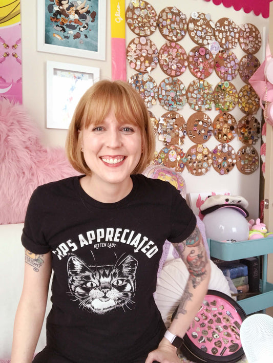 Becky sitting in front of her giant pin collection hanging on the wall and her black bubble gum ita bag to the side.